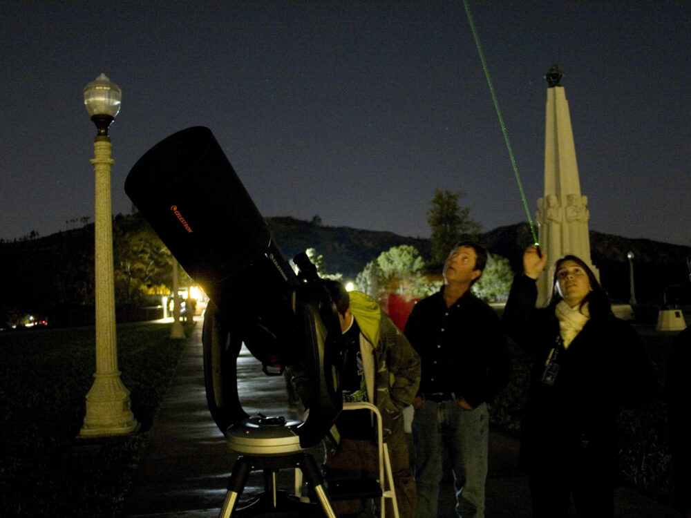 Telescope demonstrator Katy Haugland uses a laser to point out celestial wonders to Observatory patrons while standing next to a telescope on the lawn.
