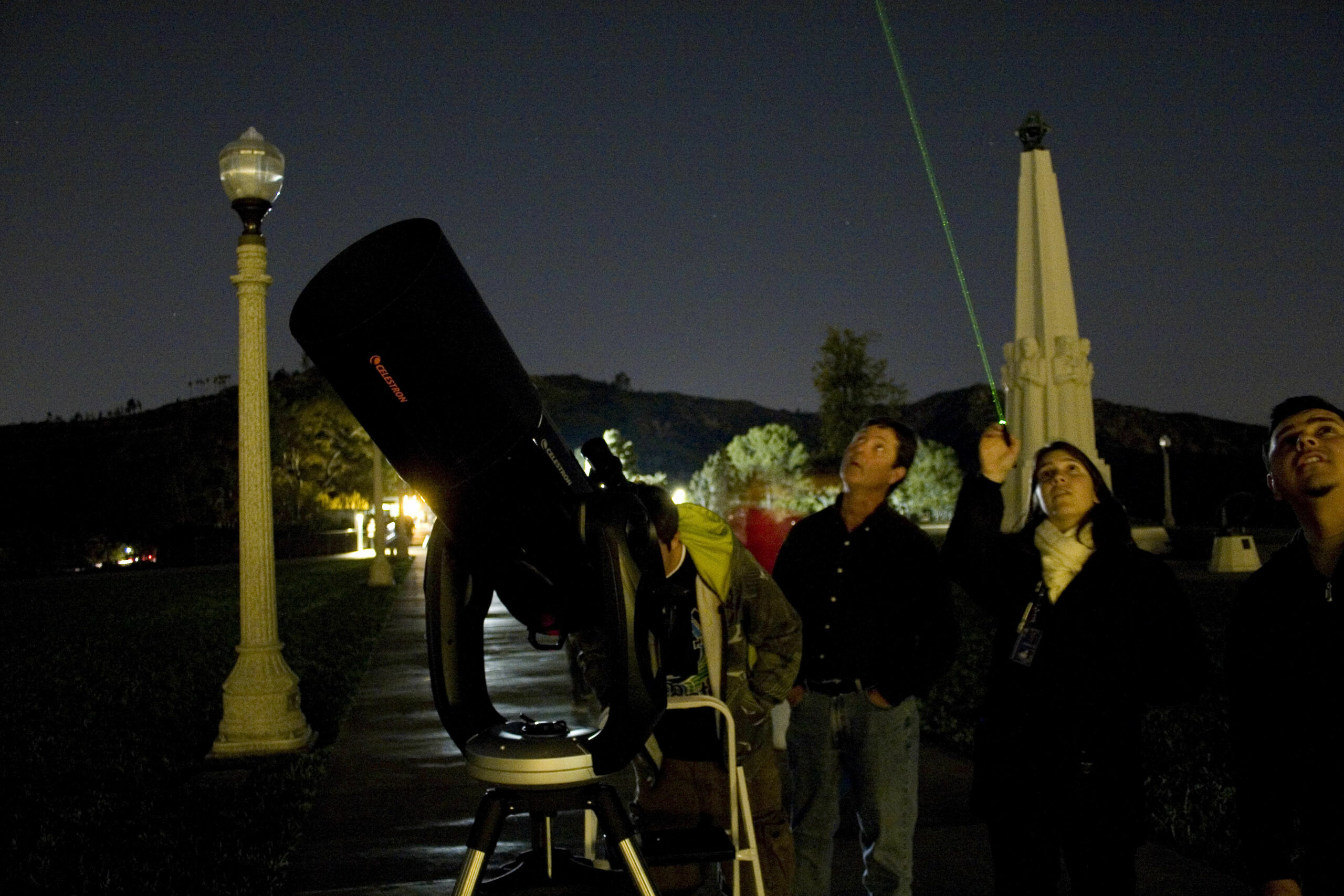 Telescope demonstrator Katy Haugland uses a laser to point out celestial wonders to Observatory patrons while standing next to a telescope on the lawn.