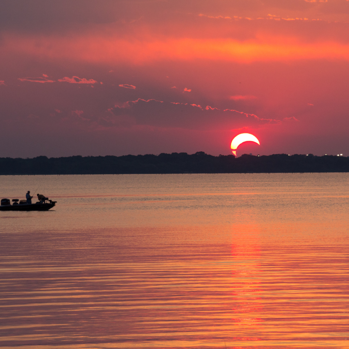 Partial eclipse along the horizon on a body of water.