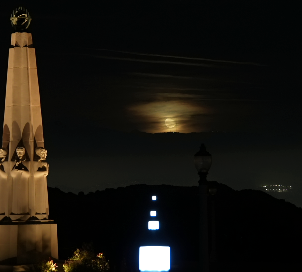 Square lanterns in a line pointing to the spot where the moon rises above the mountains.