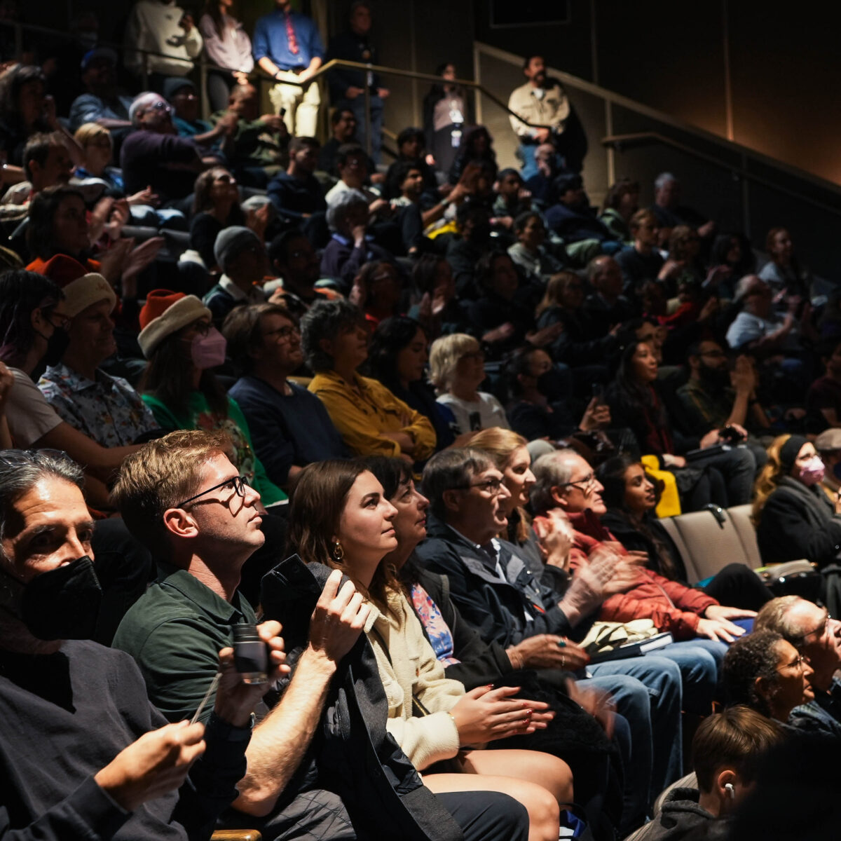 A rapt audience sit in a dim theater.