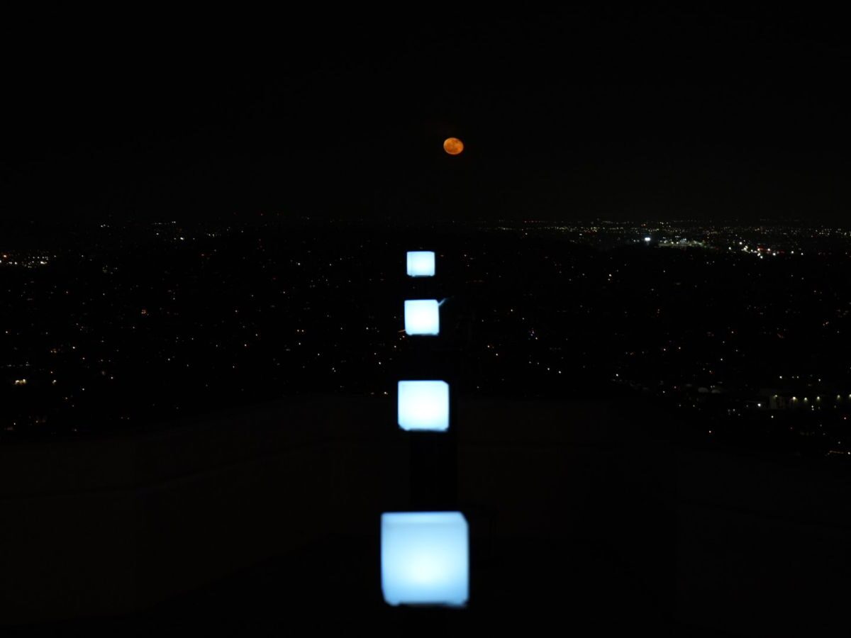 Square white lights in line with the path of a coppery red moon rise.