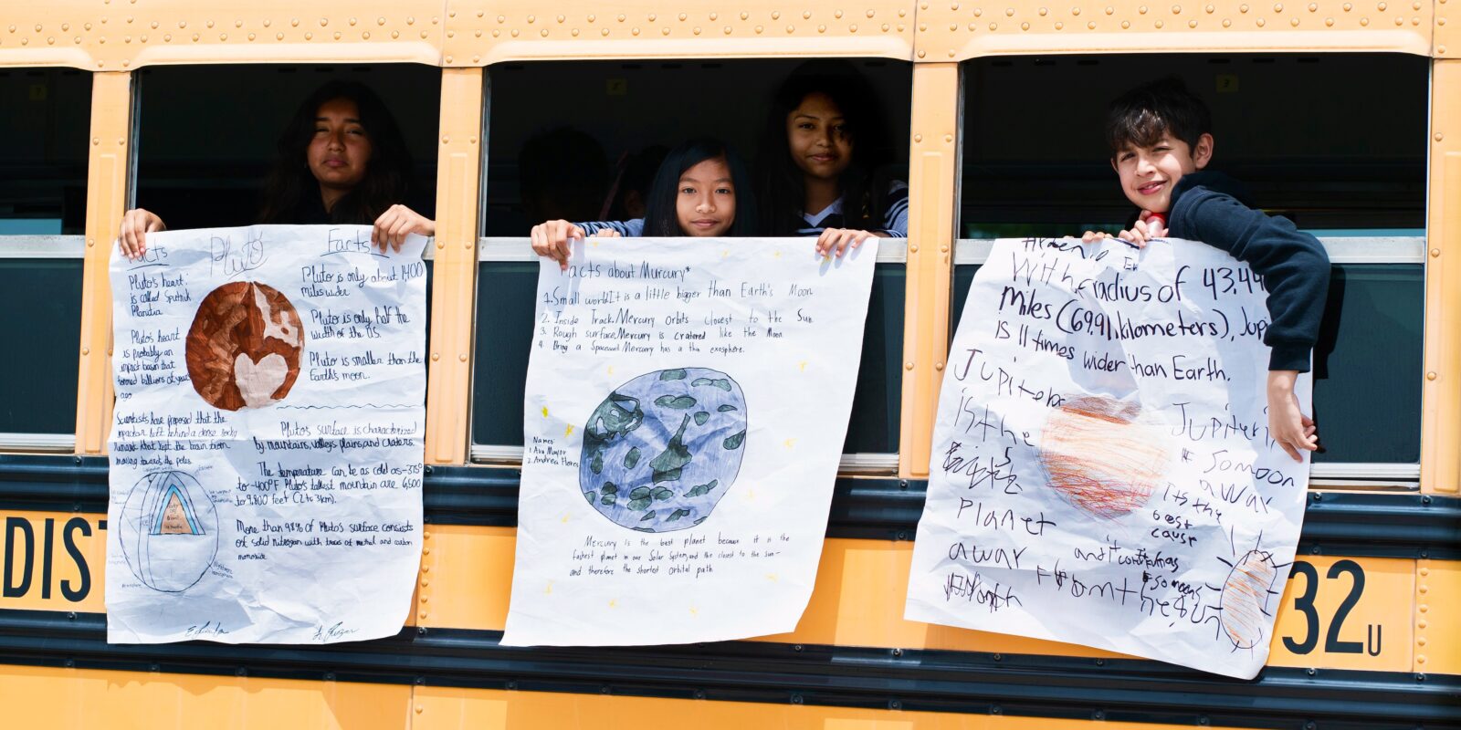 Kids hanging handmade planet posters from the school bus windows.
