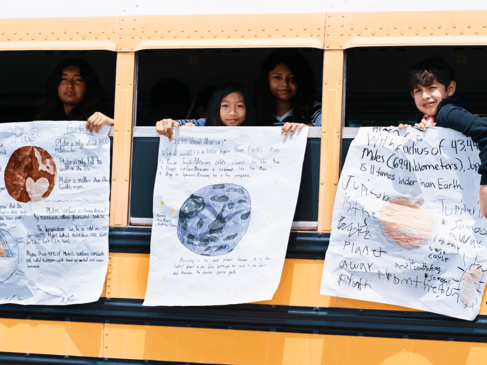 Children hanging handmade astronomy posters outside a school bus's windows.