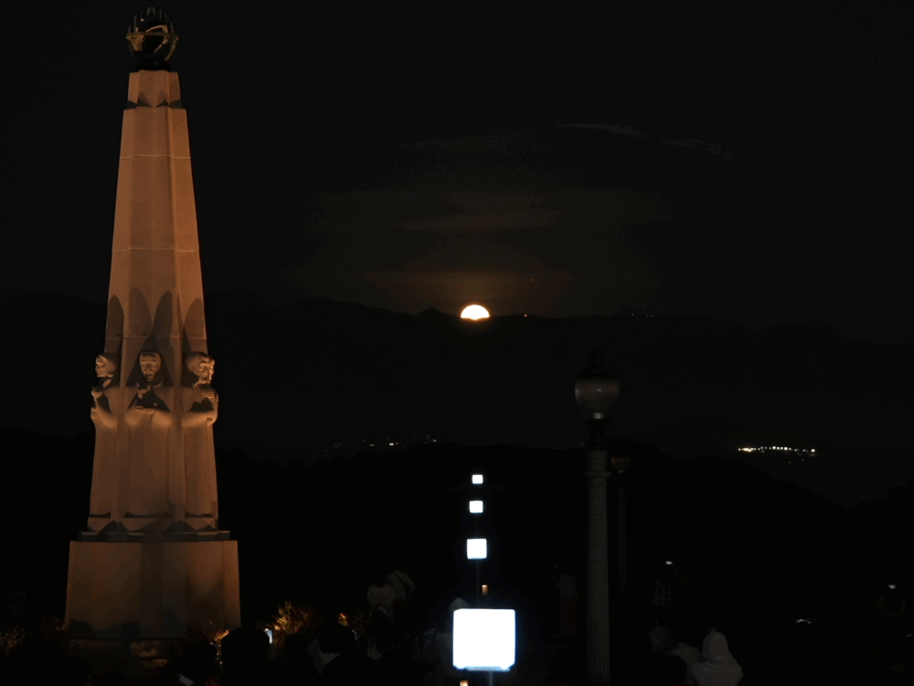 Square lights in a row lining up with a full moon rising over the mountains.