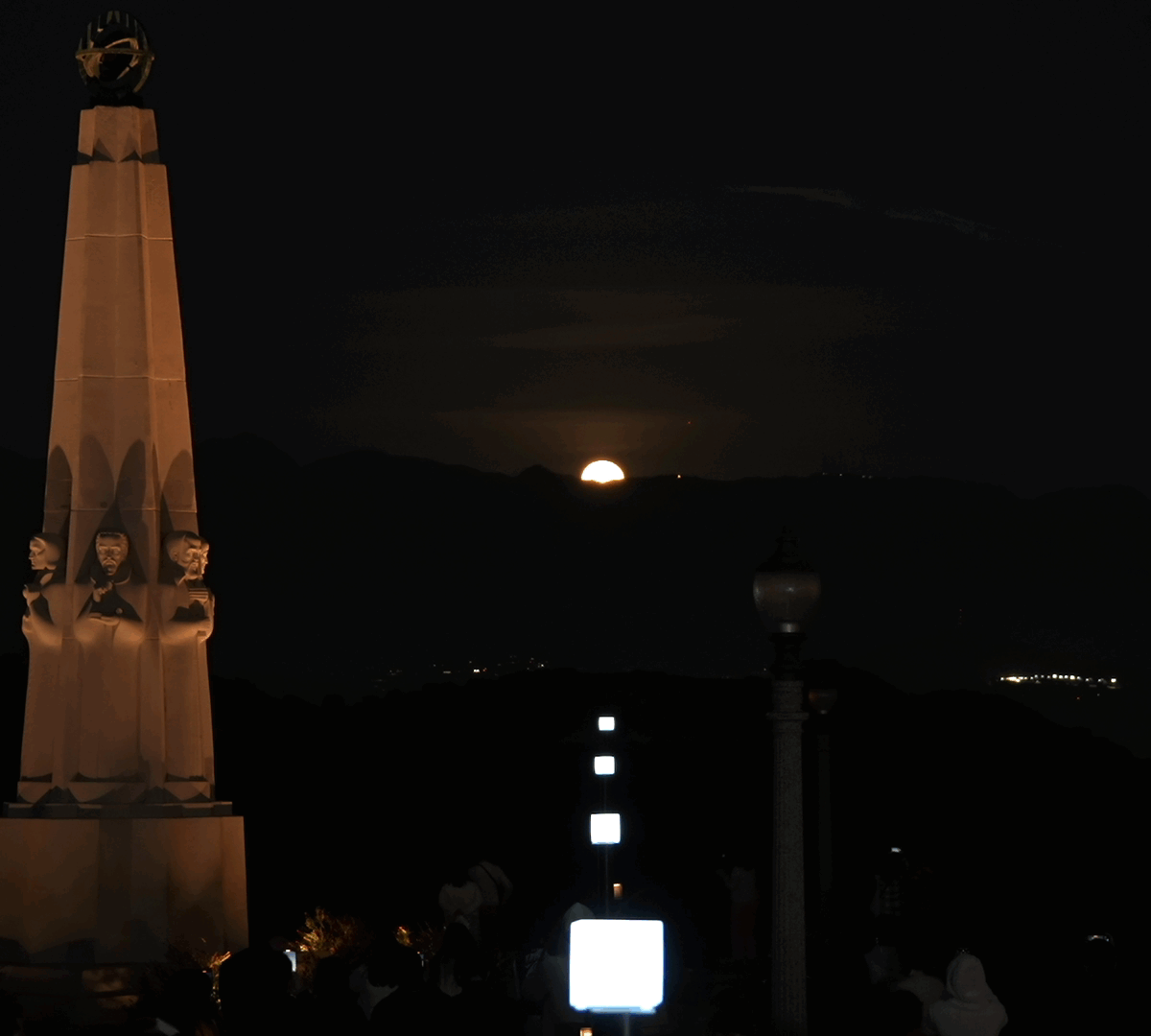 Square lights in a row lining up with a full moon rising over the mountains.