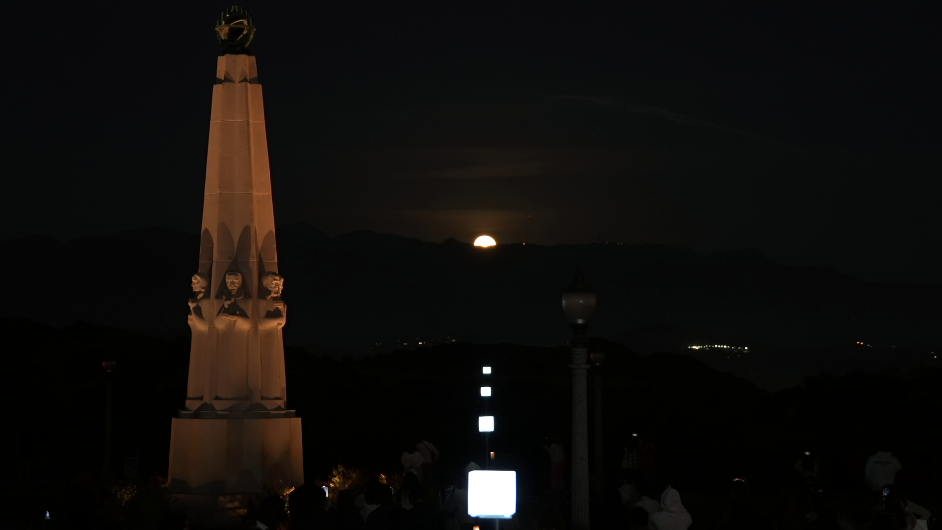 Square lights in a row lining up with a full moon rising over the mountains.