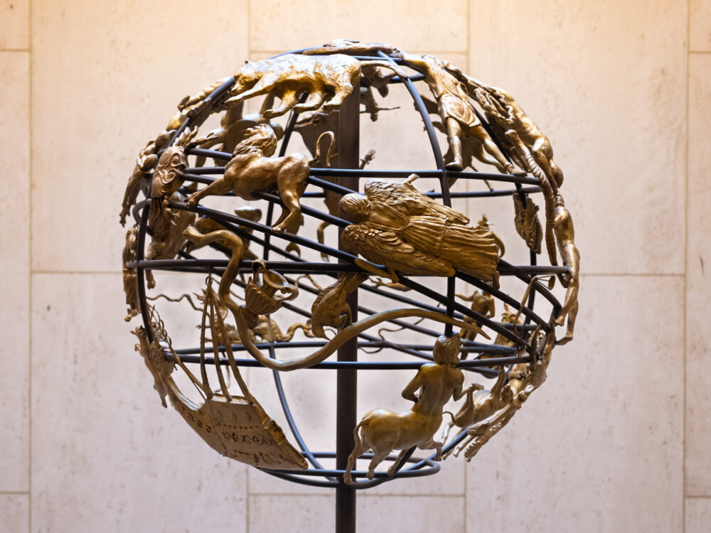A wire globe covered with bronze zodiac figures.
